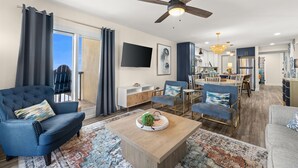A modern living room with a sofa, armchair, coffee table, and dining area. - 🌴 Oceanfront Pinnacle Port Escape | Sleeps 8 | Last Week of July Available! (Panama City Beach)