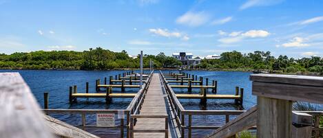 A wooden pier extending into a body of water with a warning sign, surrounded by greenery and buildings in the distance.