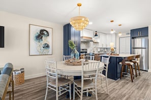 A modern kitchen with a central island, white dining set, and a large chandelier.