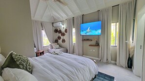 Un dormitorio con una cama grande, un televisor de pantalla plana en la pared y una ventana con cortinas.
