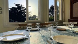 Un coin repas avec une table dressée pour quatre personnes, de grandes fenêtres et une vue sur les arbres à l’extérieur.