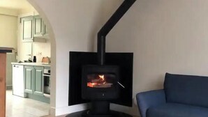 Un salon chaleureux avec un poêle à bois, un canapé bleu et une table ronde en bois.