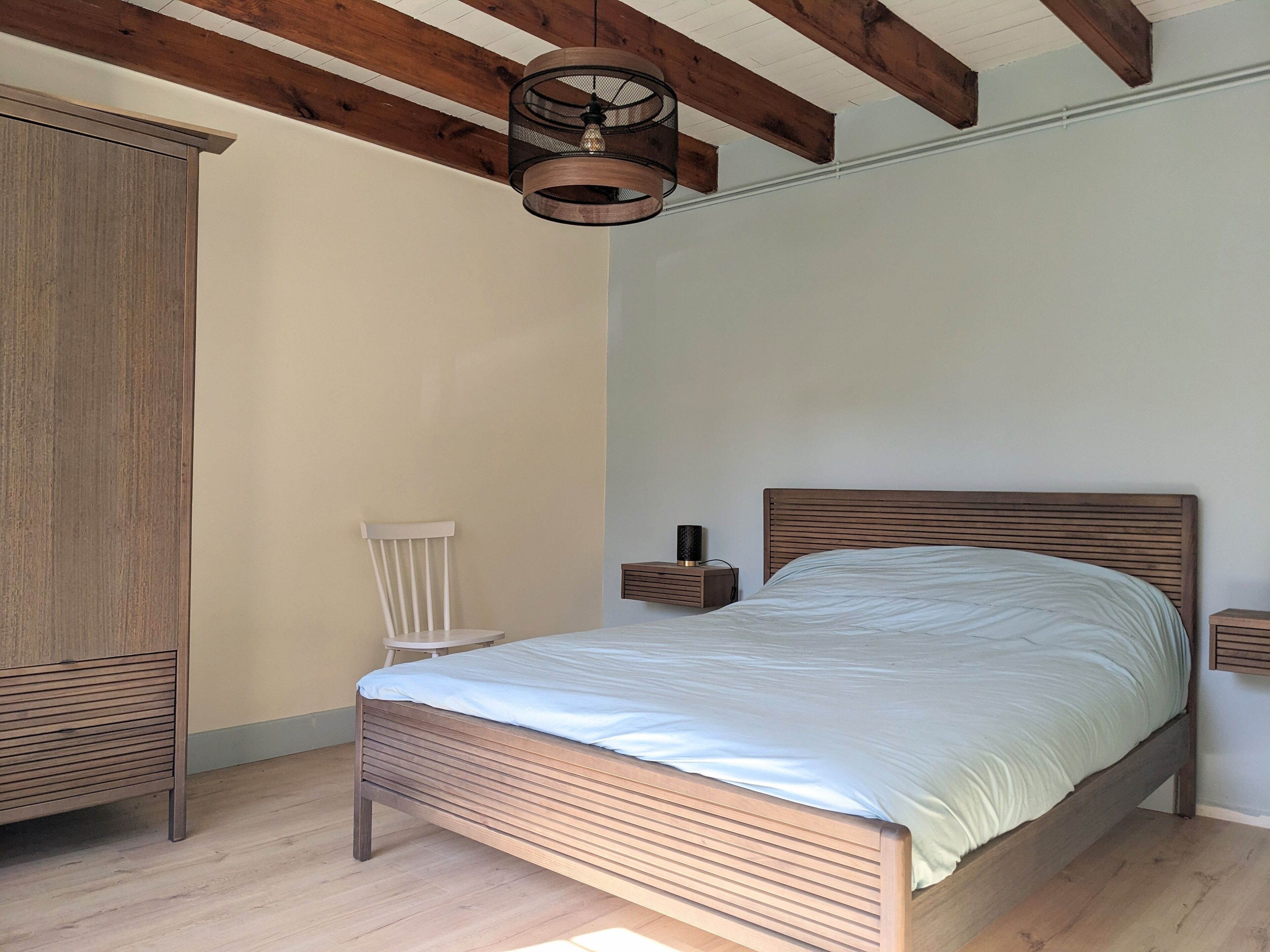 A bedroom with a wooden bed, a nightstand, a chair, and a wardrobe.