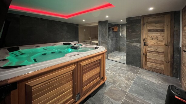 Une salle de bain moderne avec un grand bain à remous, une douche à l’italienne et une porte en bois.