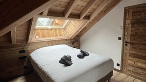 Une chambre avec un plafond en pente, des poutres en bois, un puits de lumière et un lit avec des serviettes.