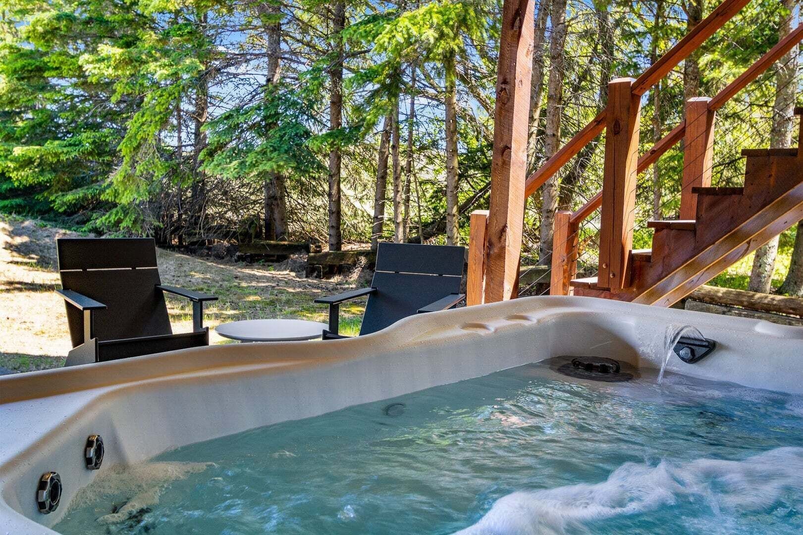 Un bain à remous avec une terrasse en bois et des chaises, entouré d’arbres.