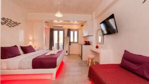 A hotel room with two beds, a desk, a TV, and a kitchenette. - The Muses of Santorini (Santorini)