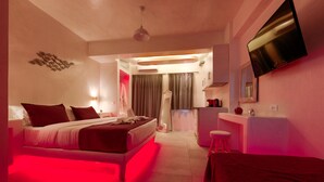 A modern hotel room with a bed, a desk, a mirror, and a TV. - The Muses of Santorini (Santorini)
