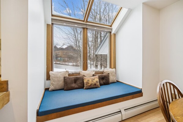 Quarto aconchegante com um assento embutido na janela, uma cadeira de madeira e vista para o exterior.