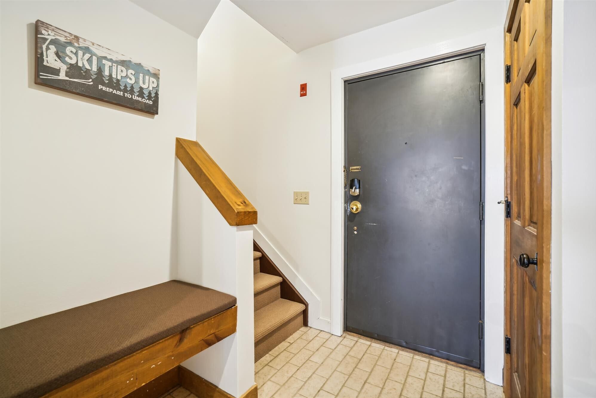 A staircase with a wooden handrail and a bench, leading to a dark door with a keyhole and a lock.