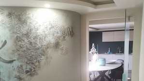 A modern kitchen with a curved wall featuring decorative patterns, a dining area with a round table and chairs, and a visible kitchen counter with appliances.