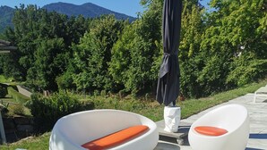 Outdoor seating with white and orange cushions, a white pedestal table, and a black umbrella.
