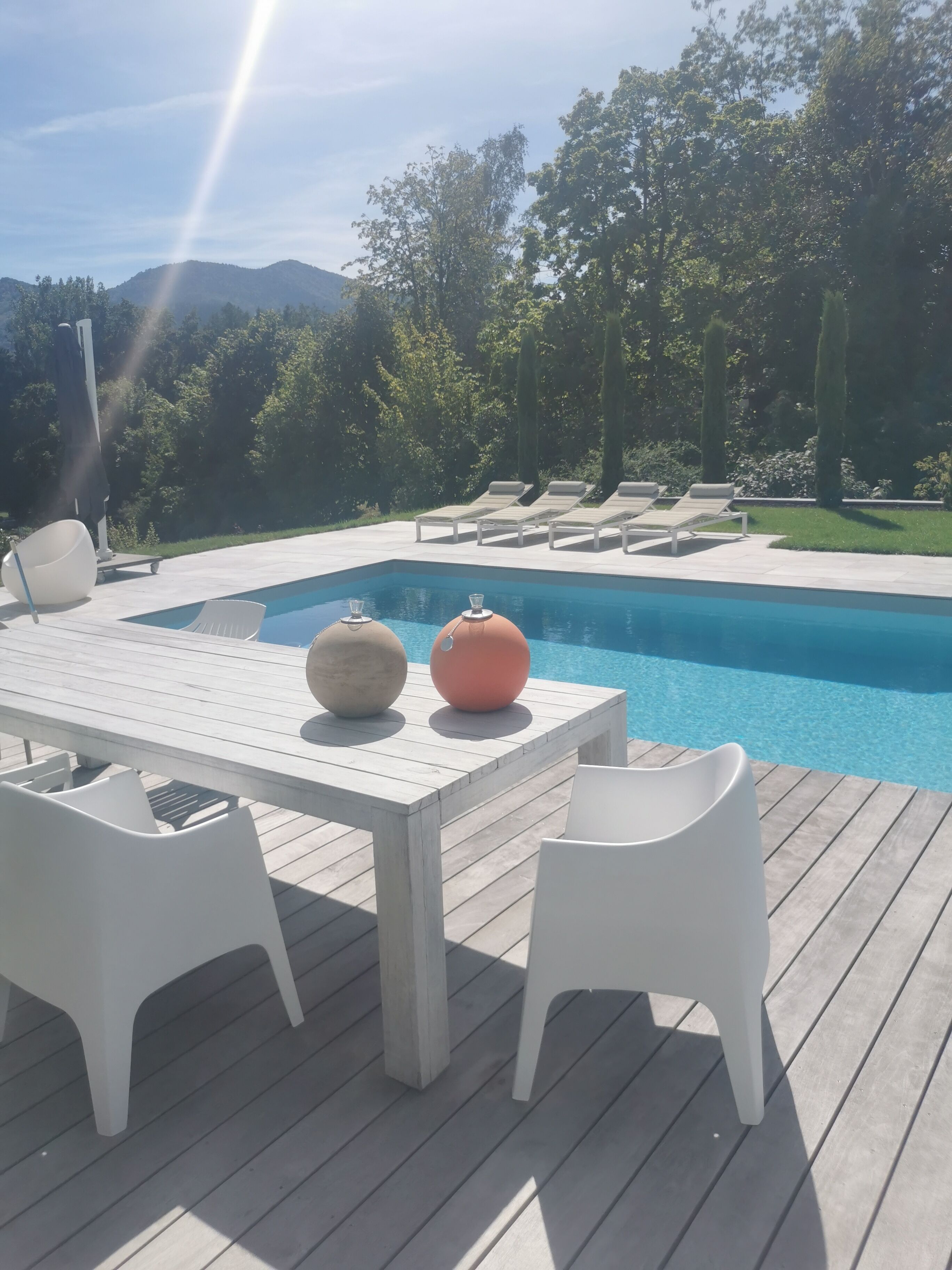 Ein Poolbereich mit Holzterrasse, weißen Liegestühlen und einem Tisch mit zwei dekorativen Vasen.