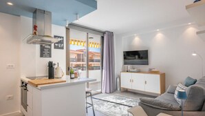 Un appartement moderne comprenant une cuisine, un coin repas et un salon. Il est équipé d’une grande fenêtre, d’un téléviseur à écran plat et d’un canapé.