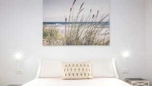 Une chambre avec un grand lit, un tableau représentant une plage accroché au mur et deux lampes de chevet.