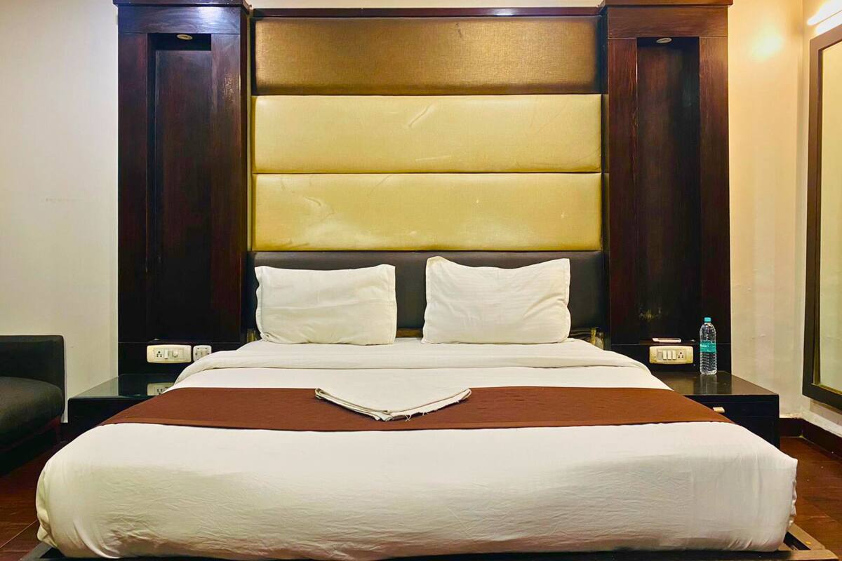 Una habitación de hotel con una cama grande, un cabecero acolchado, dos mesitas de noche y una mesita con una botella de agua.