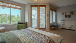 Ein Schlafzimmer mit einem großen Bett, einem Deckenventilator, einem grünen Schrank, einer Bank, einem Schminktisch und Blick ins Freie durch das Fenster.