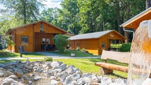 A cabin-style hotel with two wooden buildings, a stone-paved courtyard, and a waterfall feature. - 3-sterne Ferienhäuser am Bärwalder See in der Urlaubsregion Lausitzer Seenland (Boxberg/Oberlausitz)