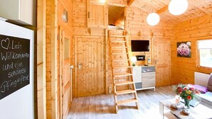A cozy wooden cabin interior with a wooden staircase, a sofa, a small table with flowers, and a TV on the wall. - 3-sterne Ferienhäuser am Bärwalder See in der Urlaubsregion Lausitzer Seenland (Boxberg/Oberlausitz)