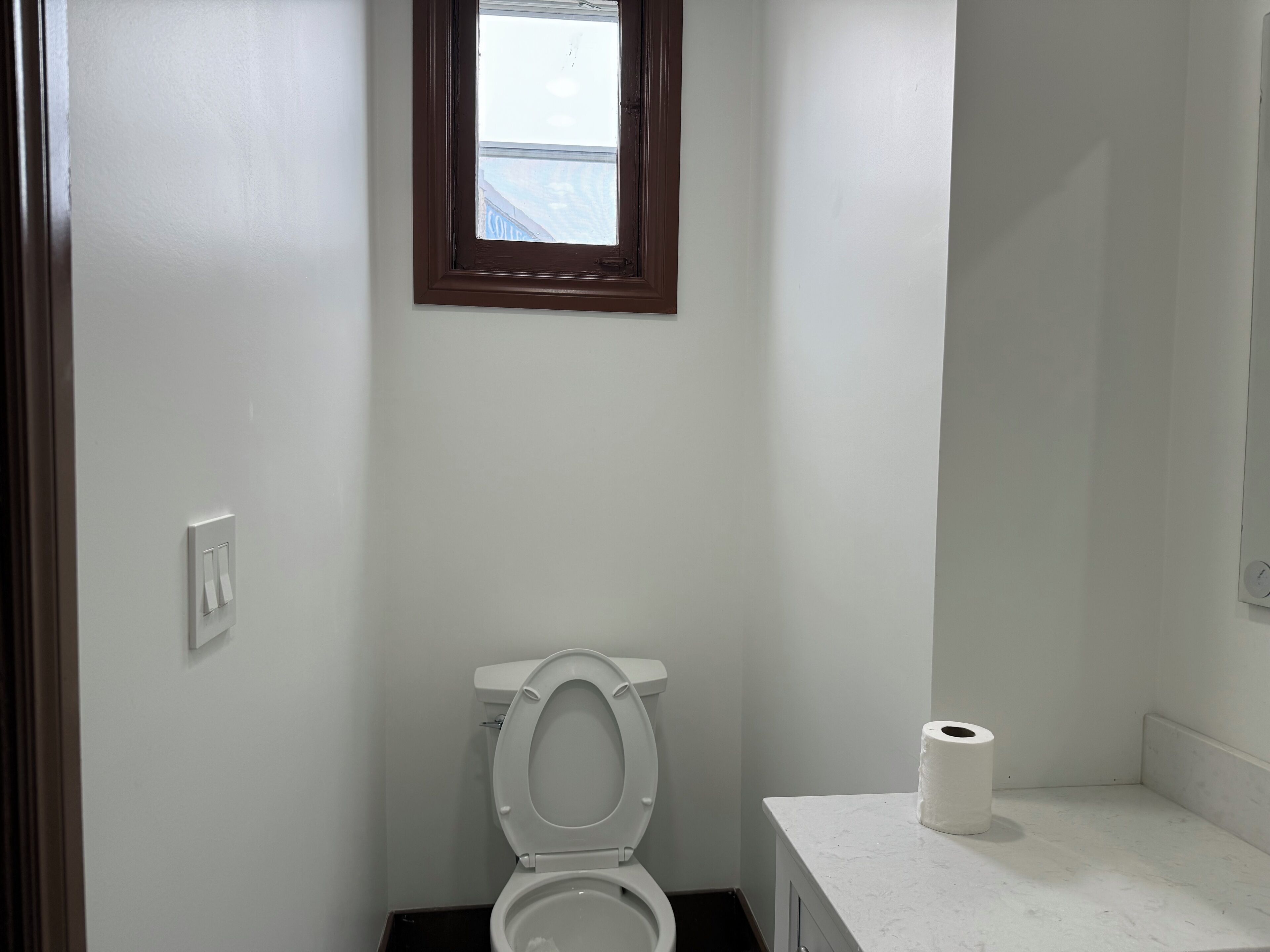 A small, clean bathroom with a toilet, a mirror, and a window.