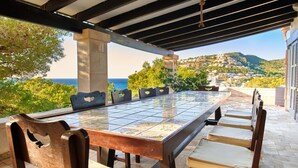 Un espace de restauration en plein air avec une table et des chaises carrelées, offrant une vue panoramique sur la mer et les collines.