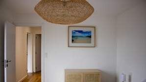 Una camera da letto con un letto, una testiera in vimini, un quadro incorniciato raffigurante una spiaggia e un armadietto in vimini.