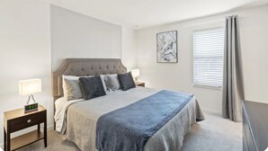 Un dormitorio con cama, mesita de noche y ventana con cortinas.