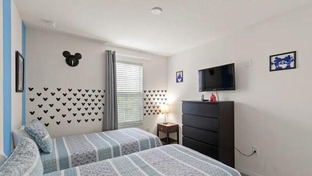 Un dormitorio con dos camas, un tocador, un televisor y adhesivos decorativos con el tema de Mickey Mouse.