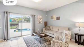Un salón con sofá, sillón, mesa de centro y vistas a una piscina a través de un ventanal corredero.