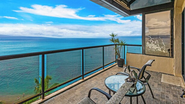 Ein Balkon mit freiem Blick auf den Ozean, einem Blumentopf und einem Glastisch mit Stühlen.