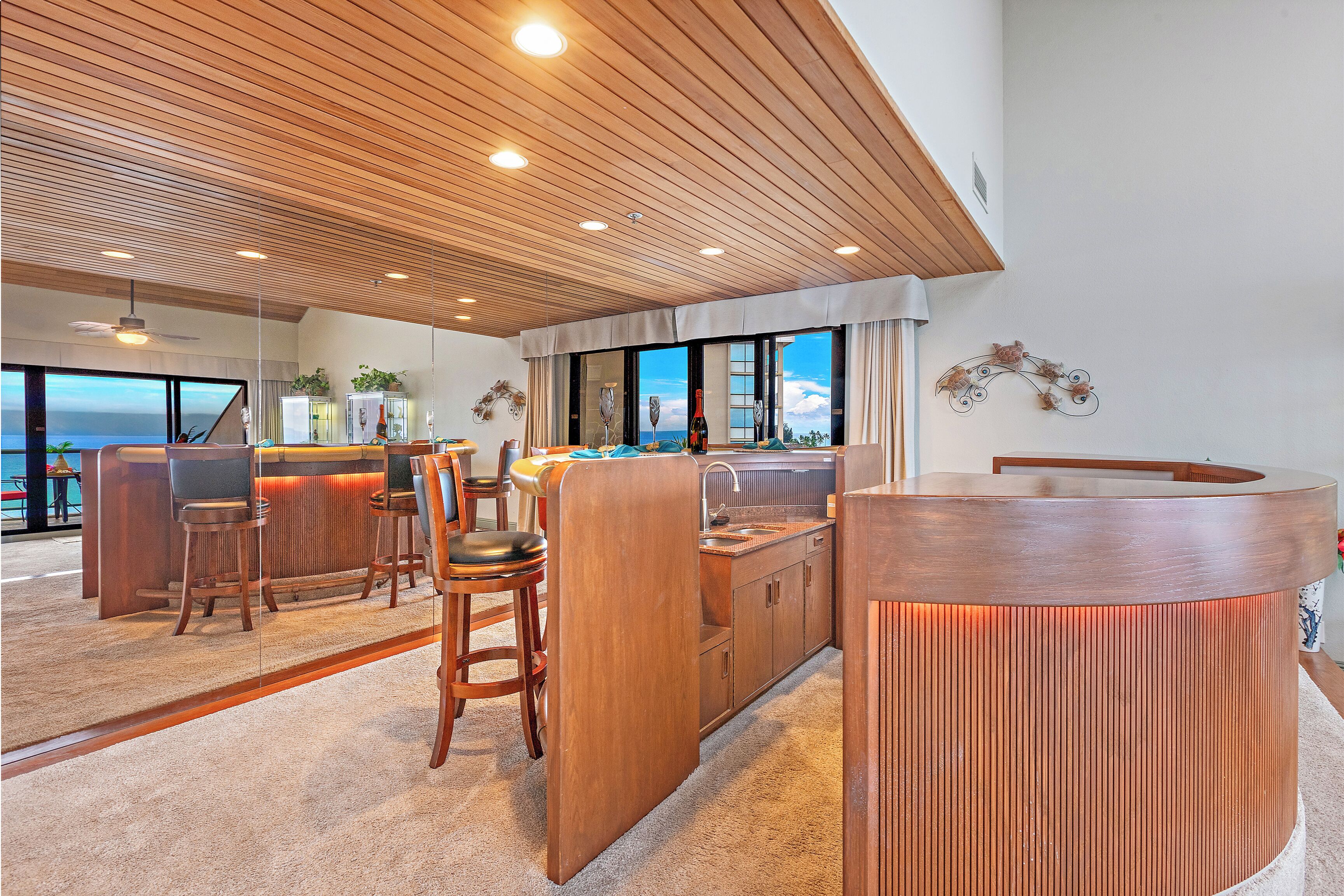 Een moderne keuken met houten kastjes, een bar en grote ramen met uitzicht op de oceaan.