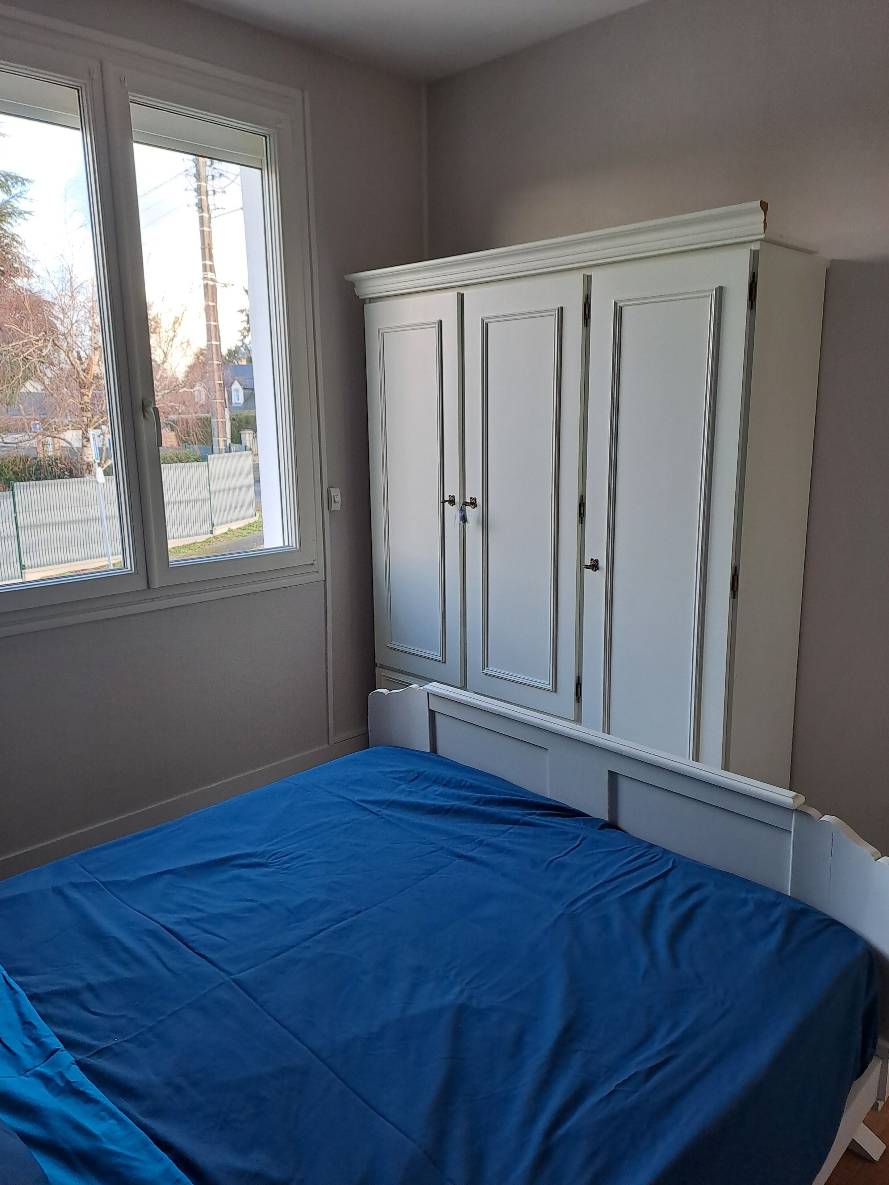 Un dormitorio con cama, ventana y armario blanco.