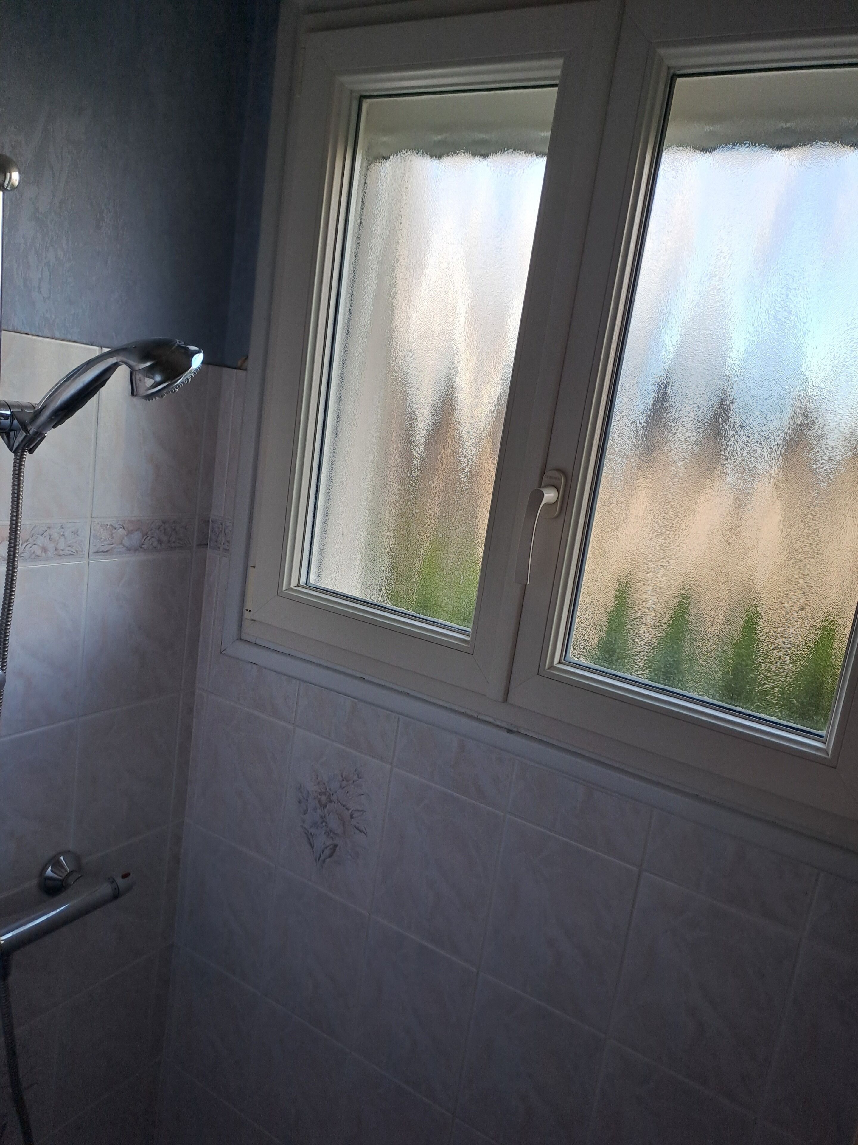 A bathroom with a shower, a window with frosted glass, and a tiled wall.