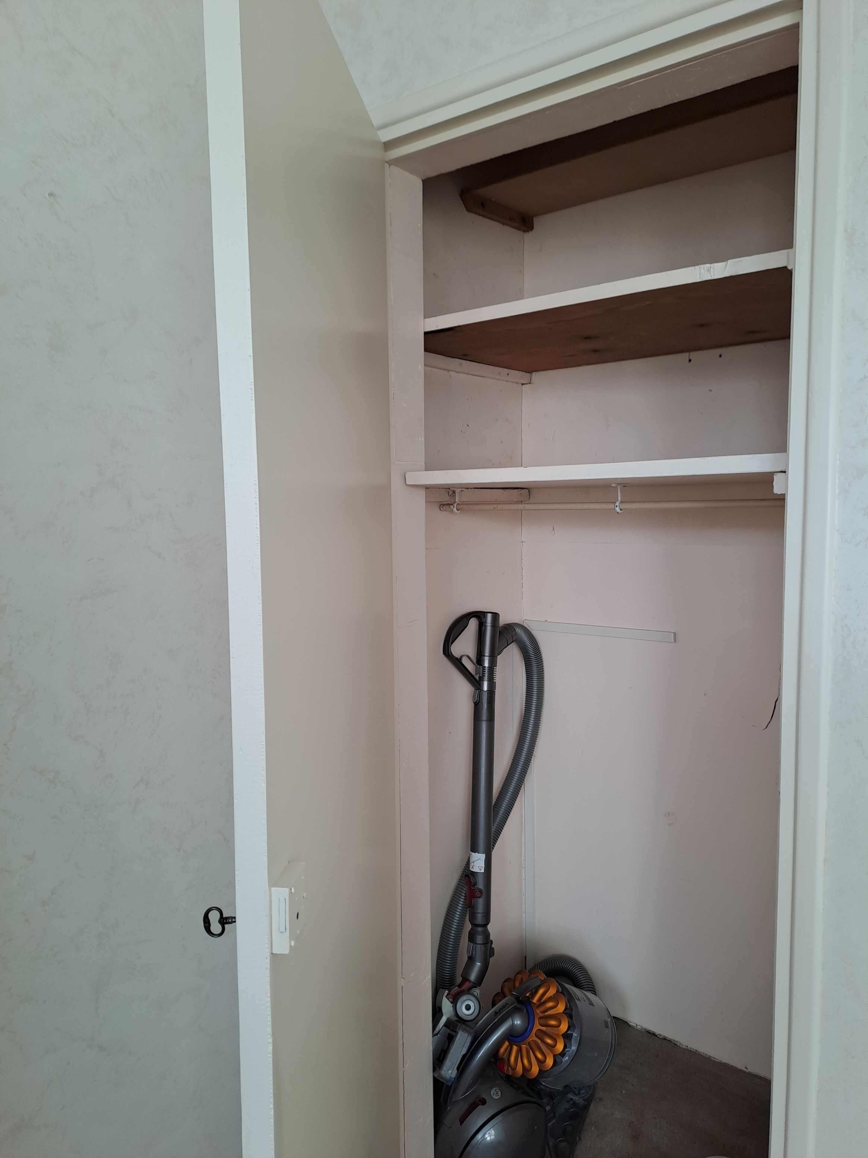 Une pièce dotée d’un aspirateur encastré, d’une porte blanche et d’une étagère en bois.