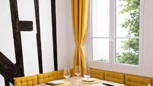 A dining area with a wooden table, yellow cushioned bench seating, and a window with curtains. - A 2 pas du Panthéon en Plein Cœur du Quartier Latin (Paris)