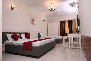 A hotel room with a large bed, a desk, a chair, a ceiling fan, and a wall-mounted TV.