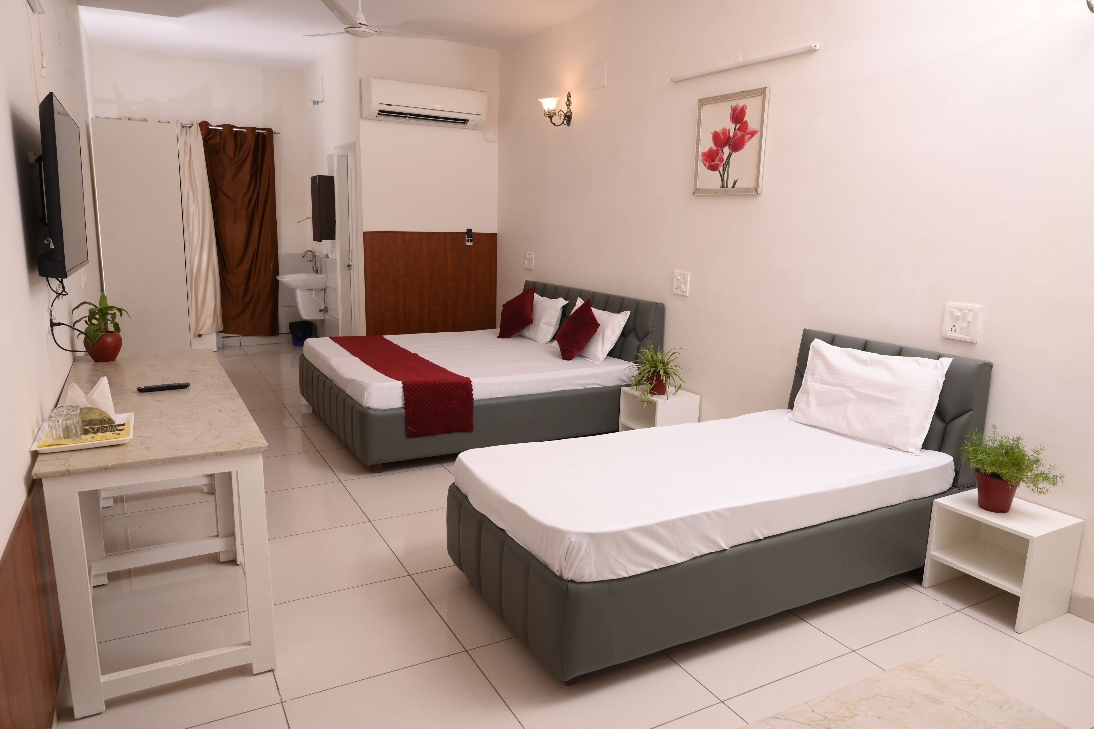 A modern hotel room with two beds, a desk, a bathroom, and a small potted plant.