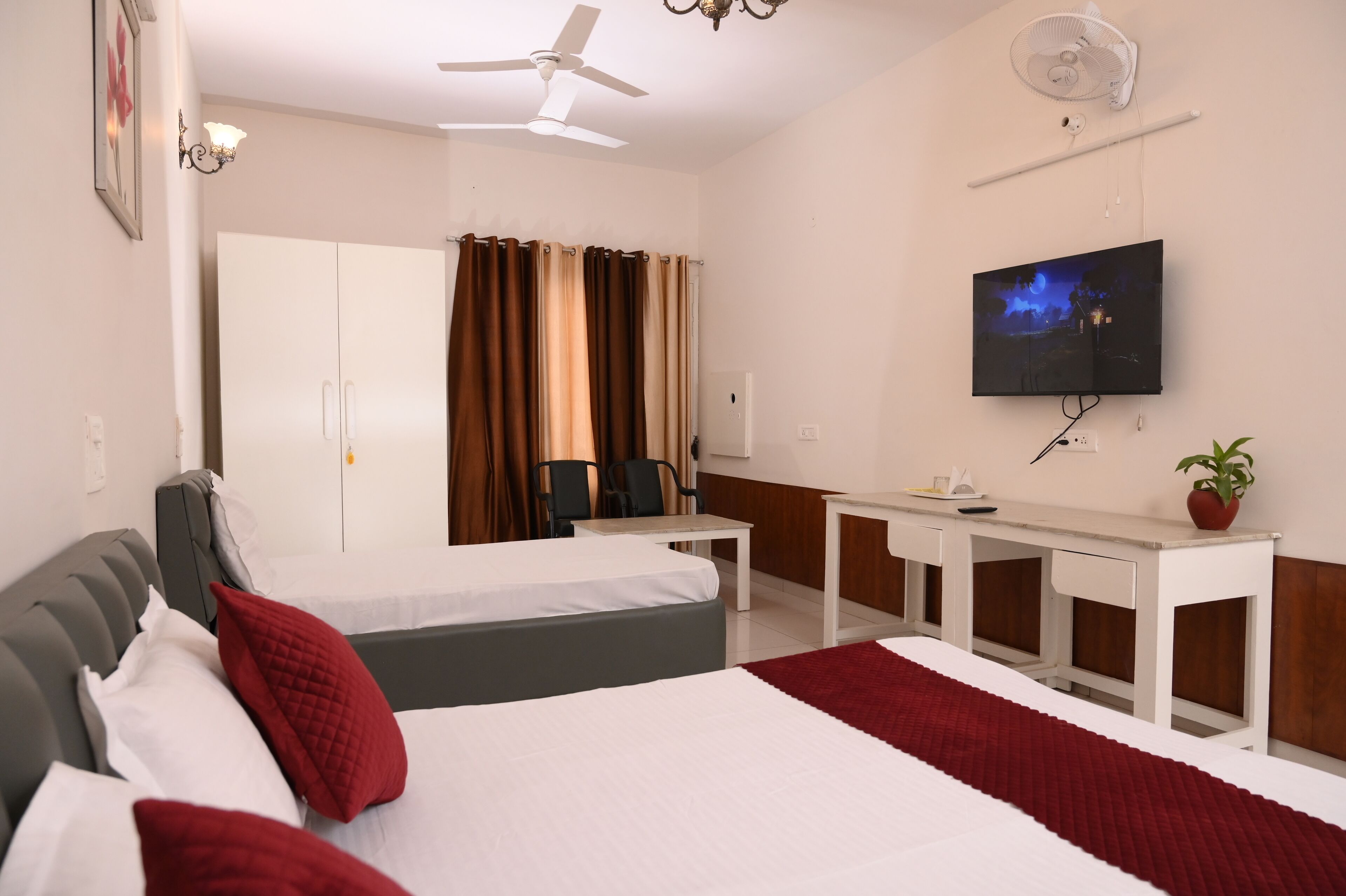 A hotel room with a bed, a desk, a chair, a TV, and a ceiling fan.