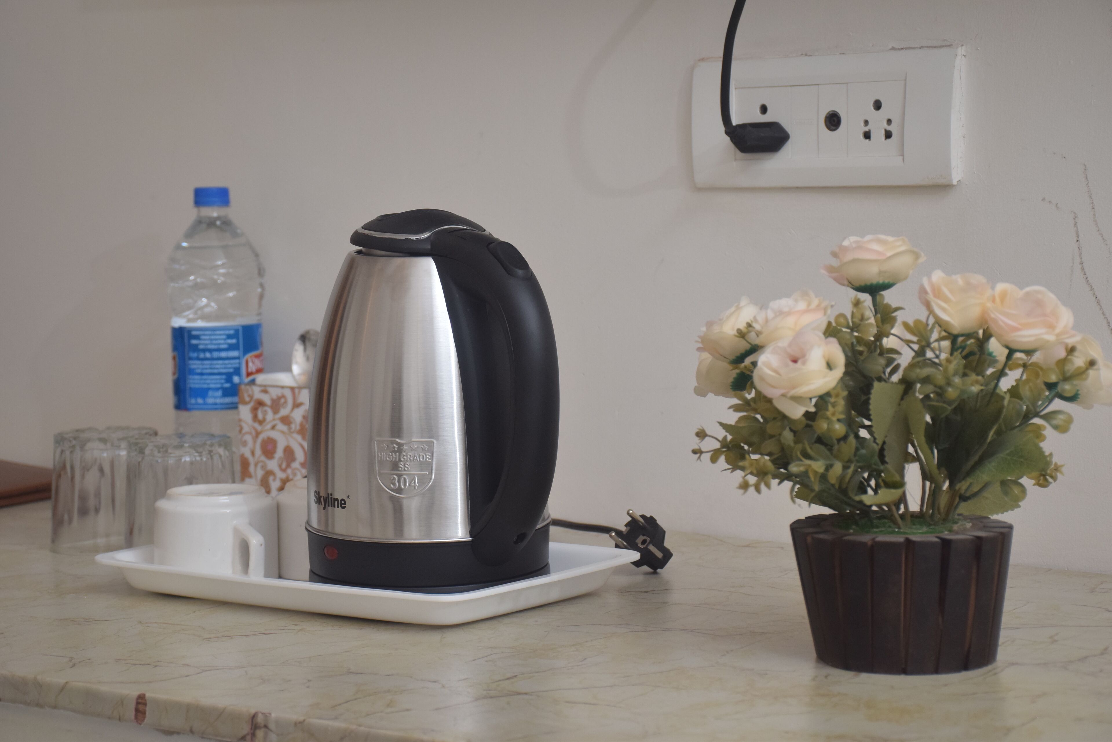 A kitchen counter with a kettle, a water bottle, a cup, and a potted plant.