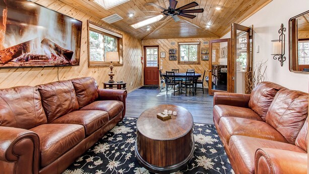 A spacious living room with leather sofas, a coffee table, and a fireplace. There is a dining area with a table and chairs, and a ceiling fan. - Red Rocks Retreat ~ Hot Tub, Game Room, Views, Privacy (Morrison)