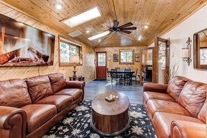 A spacious living room with leather sofas, a coffee table, and a fireplace. There is a dining area with a table and chairs, and a ceiling fan. - Red Rocks Retreat ~ Hot Tub, Game Room, Views, Privacy (Morrison)