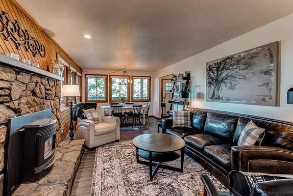 A cozy living room with a fireplace, leather sofa, and a dining area with a table and chairs. - Red Rocks Retreat ~ Hot Tub, Game Room, Views, Privacy (Morrison)