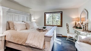 Une chambre avec un grand lit, une commode, une chaise et une fenêtre donnant sur des arbres.