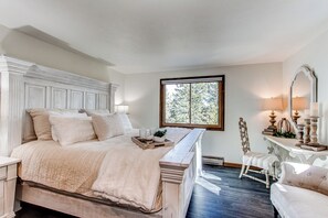 A bedroom with a large bed, a dresser, a chair, and a window with a view of trees. - Morrison Retreat ~ 15 Min To Red Rocks Amphitheatre ~ Hot Tub, Game Room, Views (Morrison)