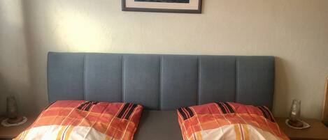 Un lit avec une tête de lit bleue, deux oreillers à motifs écossais et un tableau encadré représentant un navire accroché au mur.