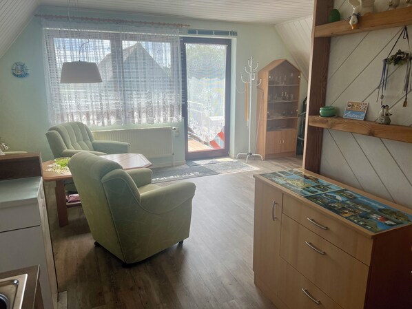 A cozy living room with a sofa, a wooden cabinet with drawers, a table, and a window with lace curtains. - An der Wiese 1 für 2 Gäste Inkl. Bettw., Wlan, Südbalkon und Parkplatz am Haus (Prerow)