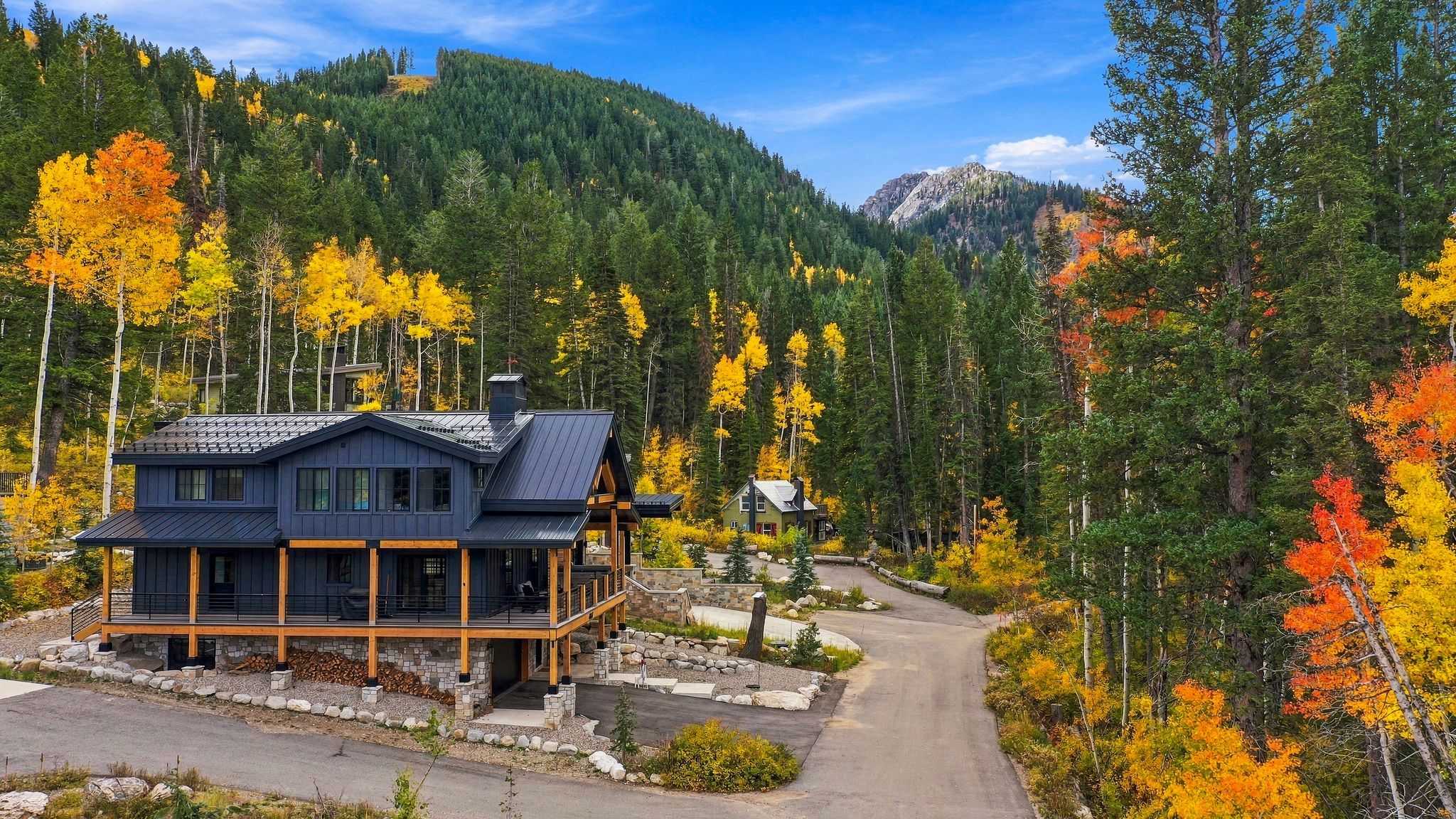A cabin with a stone foundation, a wooden deck, and a mountain backdrop.