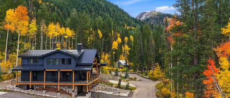 A cabin with a stone foundation, a wooden deck, and a mountain backdrop.