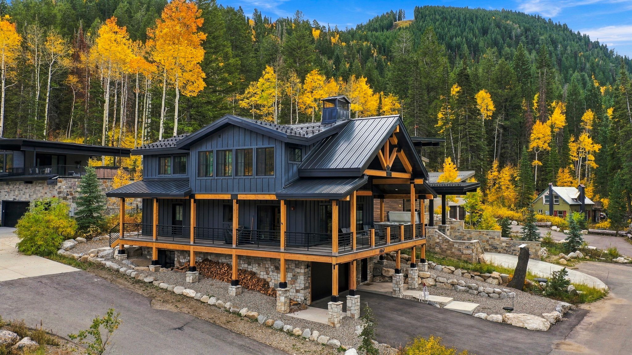 A modern two-story lodge with a stone foundation, wooden deck, and a large porch area.