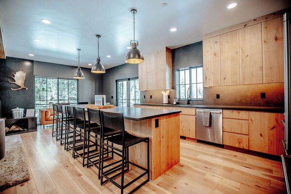 A modern kitchen with a central island, bar stools, wooden cabinets, and pendant lighting.